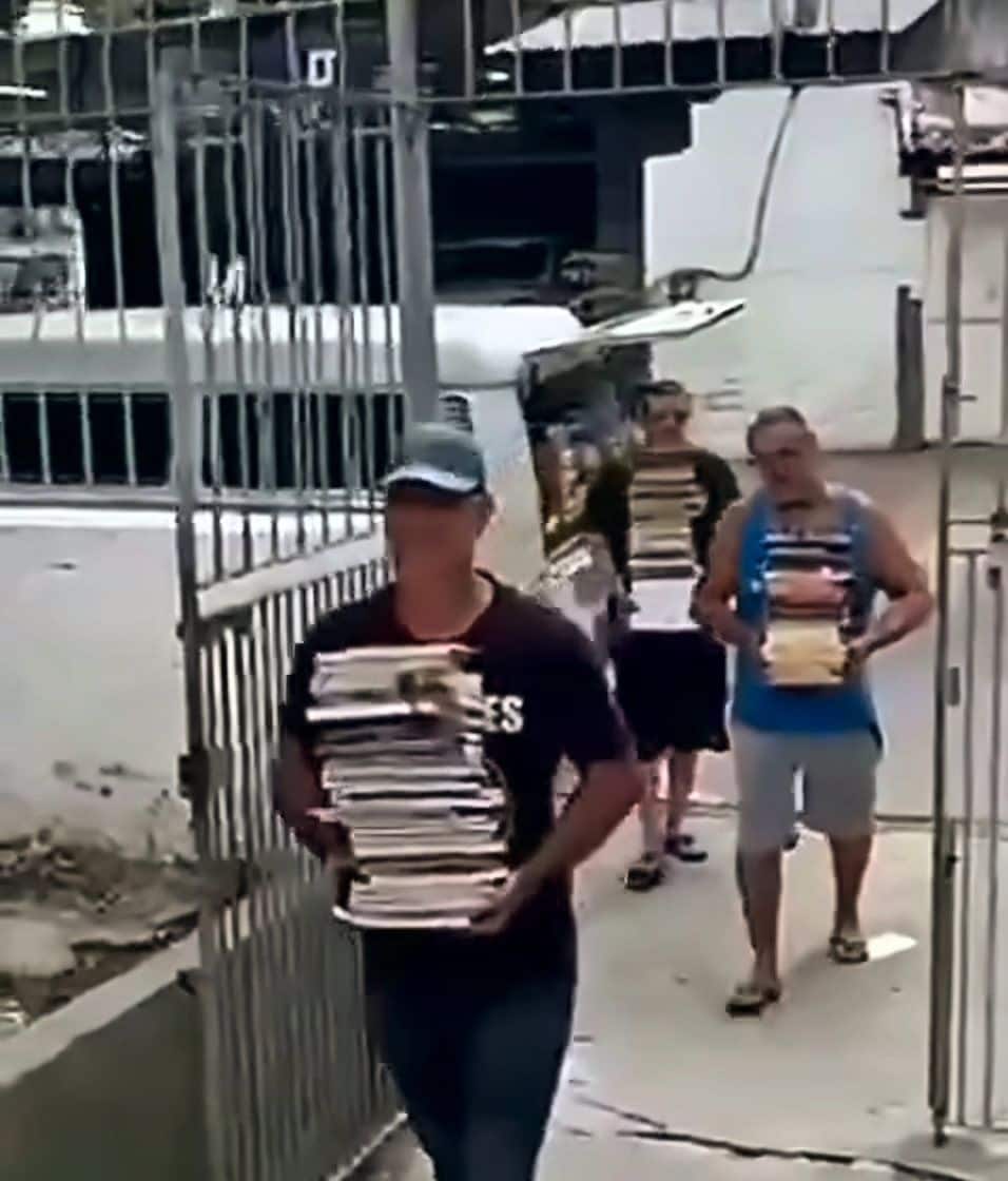 Voluntários atravessam um portão carregando pilhas de livros para doação