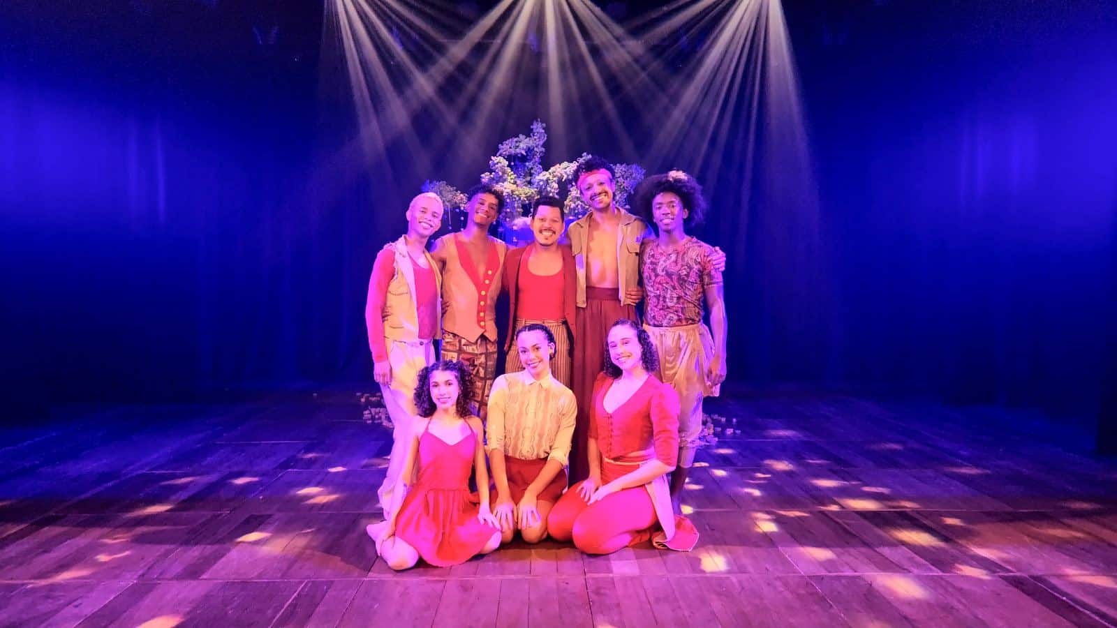 Elenco do Pé de Cachimbo no palco do Teatro da UFF, sob luz azul e rosa