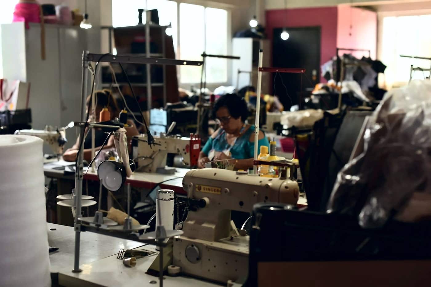 Oficina de costura com várias máquinas e pessoas trabalhando