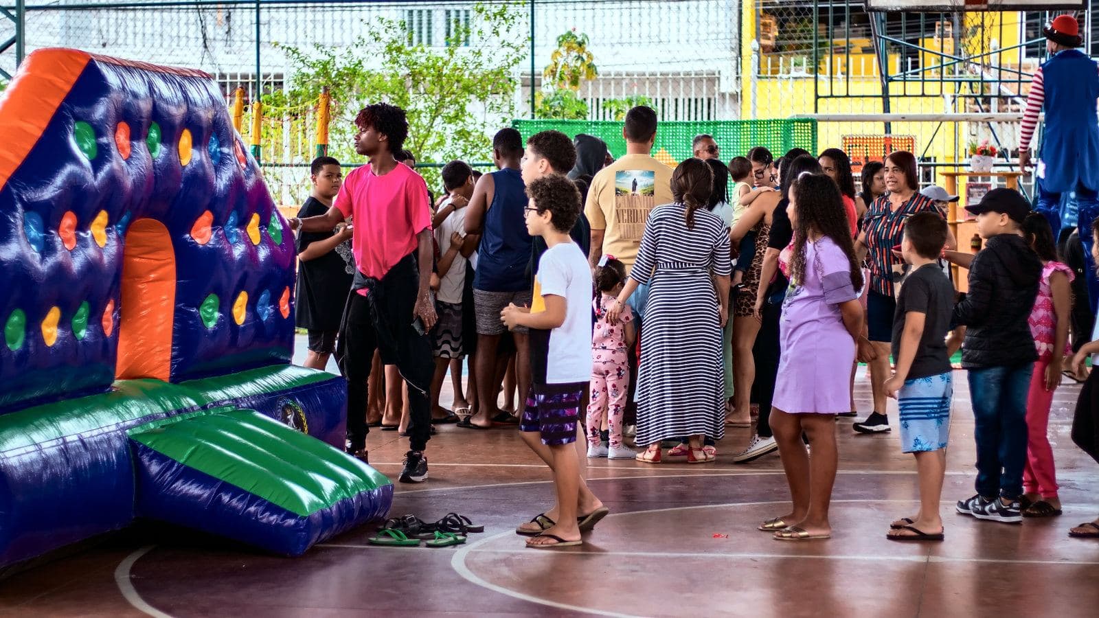 Crianças e famílias reunidas na quadra da Ilha da Conceição, ao lado de um brinquedo inflável colorido, no Dia das Crianças.