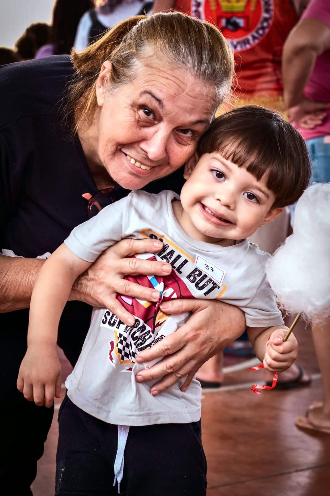 Senhora abraça por trás um menino sorridente com algodão-doce
