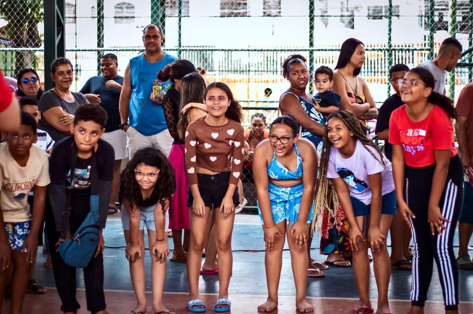Crianças, jovens e adultos curvados sorrindo para a câmera na quadra