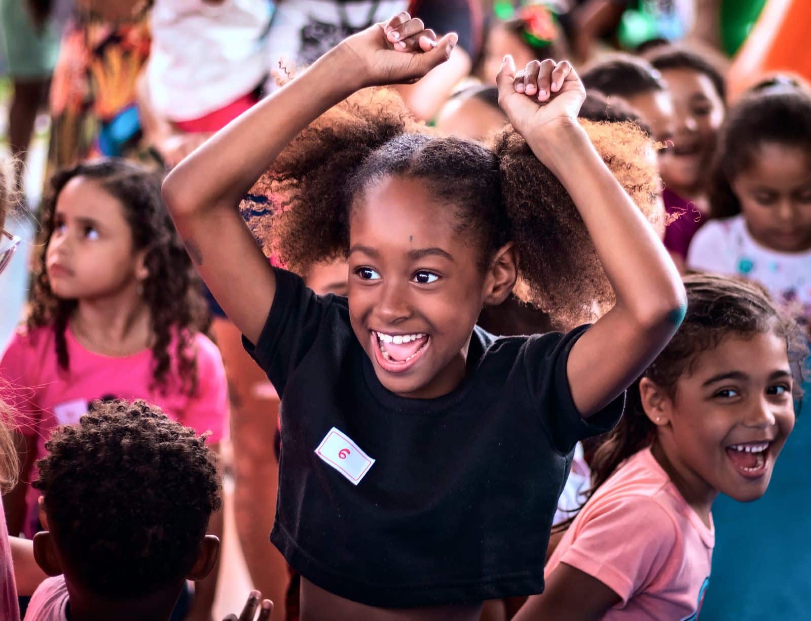 Menina dança de braços levantados, rindo, no meio da roda