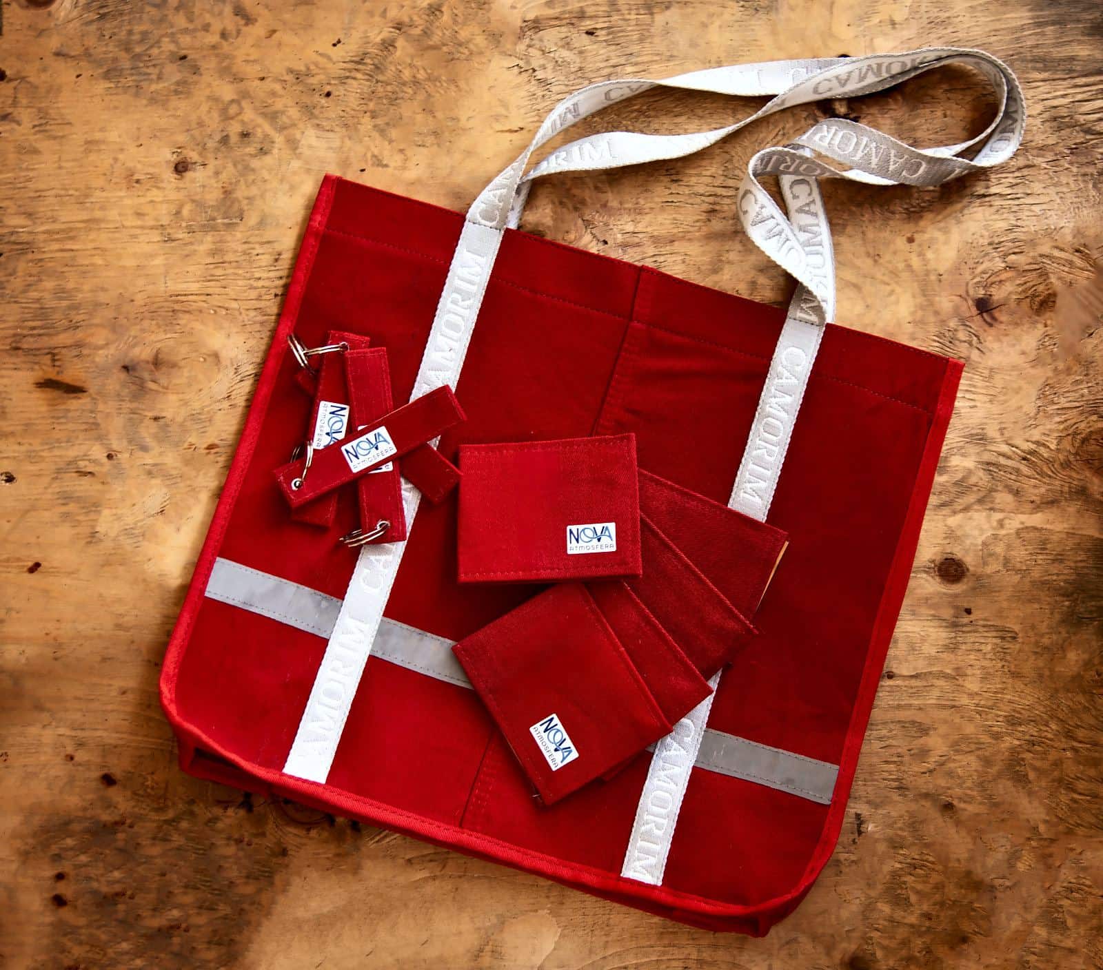 Ecobag e carteirinhas vermelhas feitas de macacões, sobre uma mesa de madeira